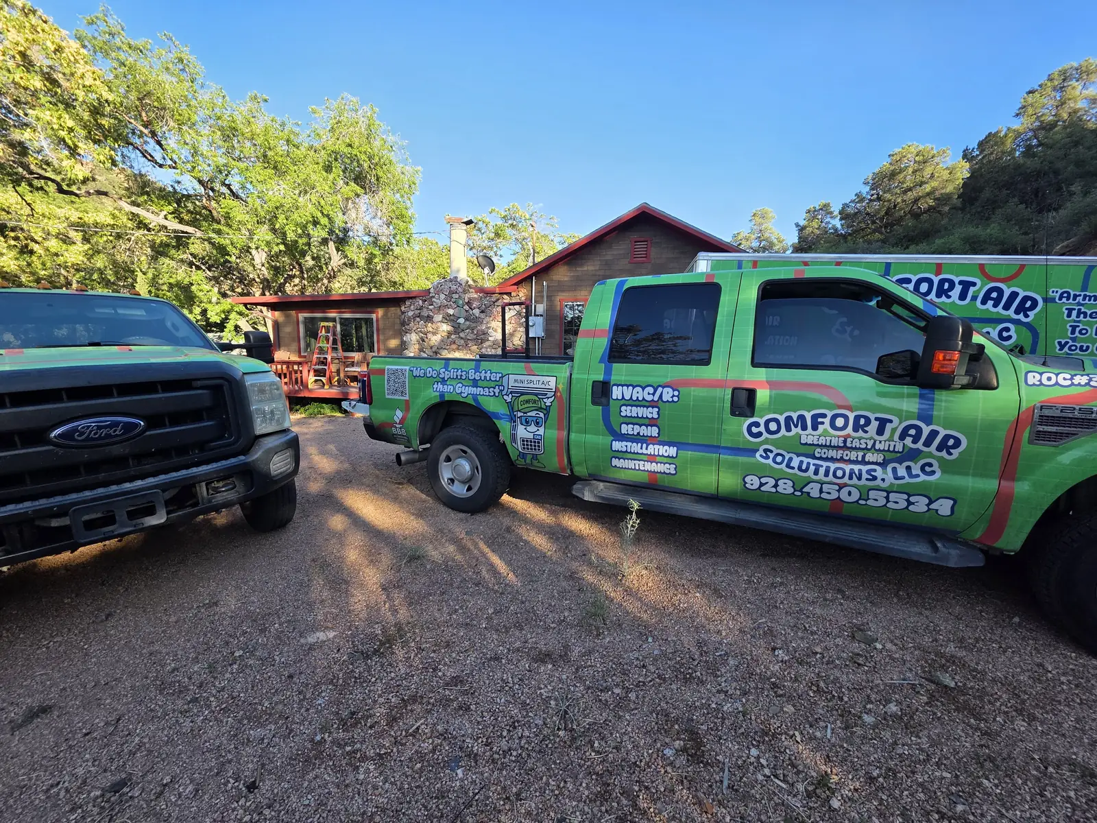 Two Comfort Air Solutions trucks parked at a hillside property