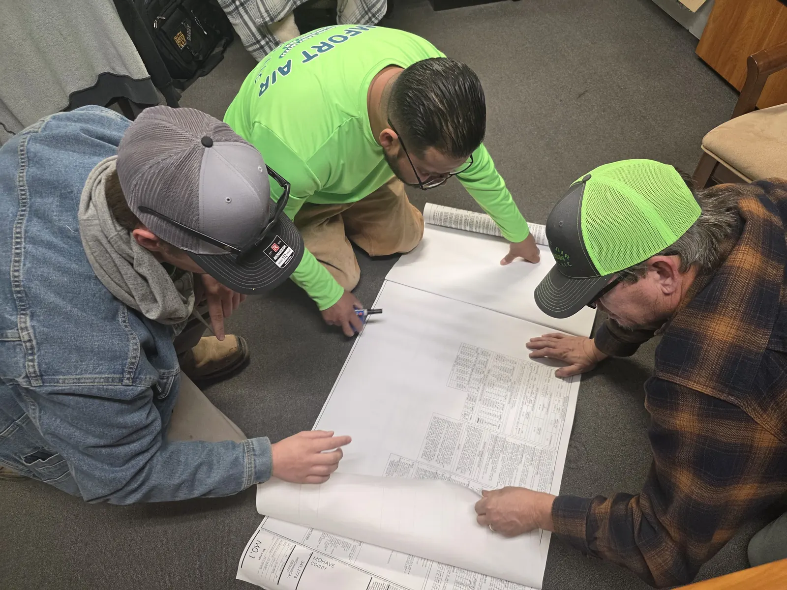 Comfort Air Solutions team reviewing construction plans on the floor with a builder