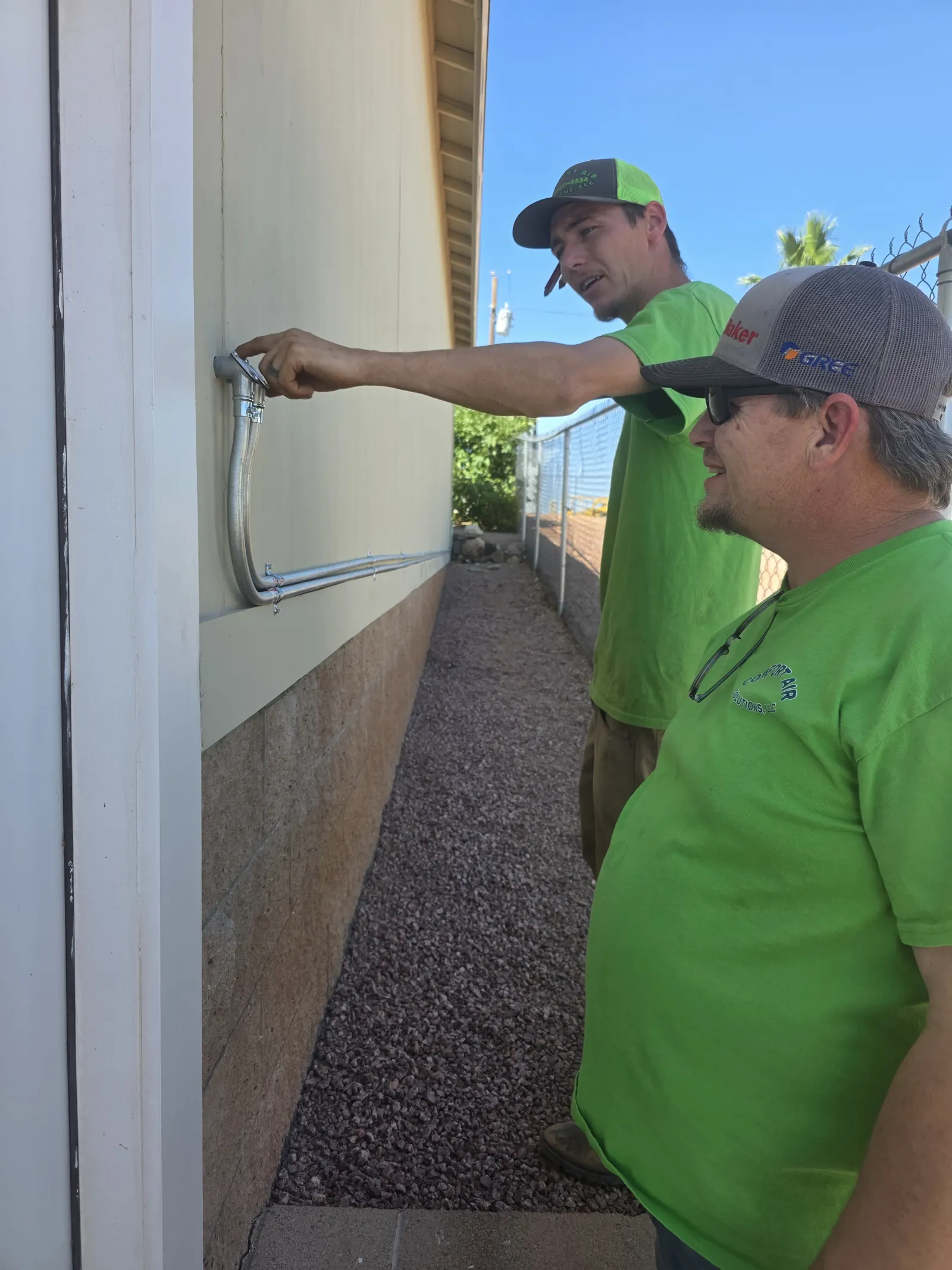 Two CAS technicians checking a line at the exterior wall of a home