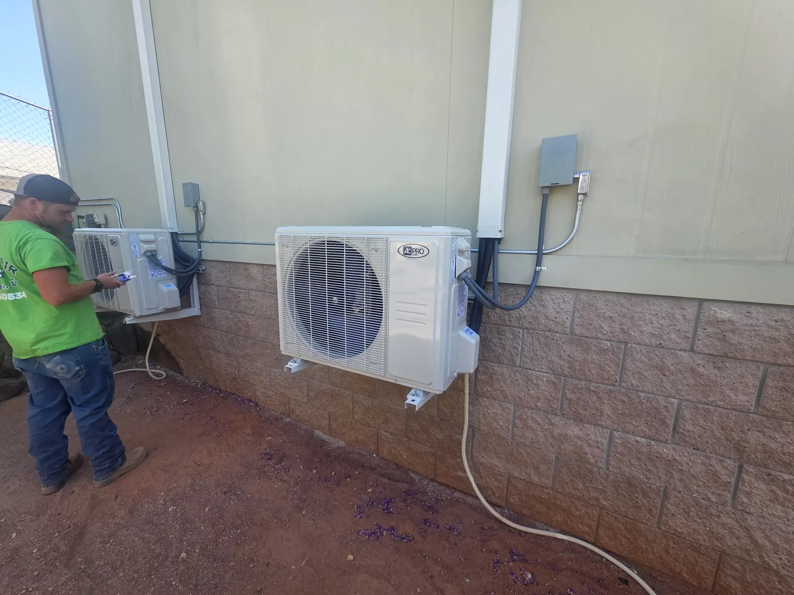 Technician working on a newly installed ductless mini split outdoor unit beside a home