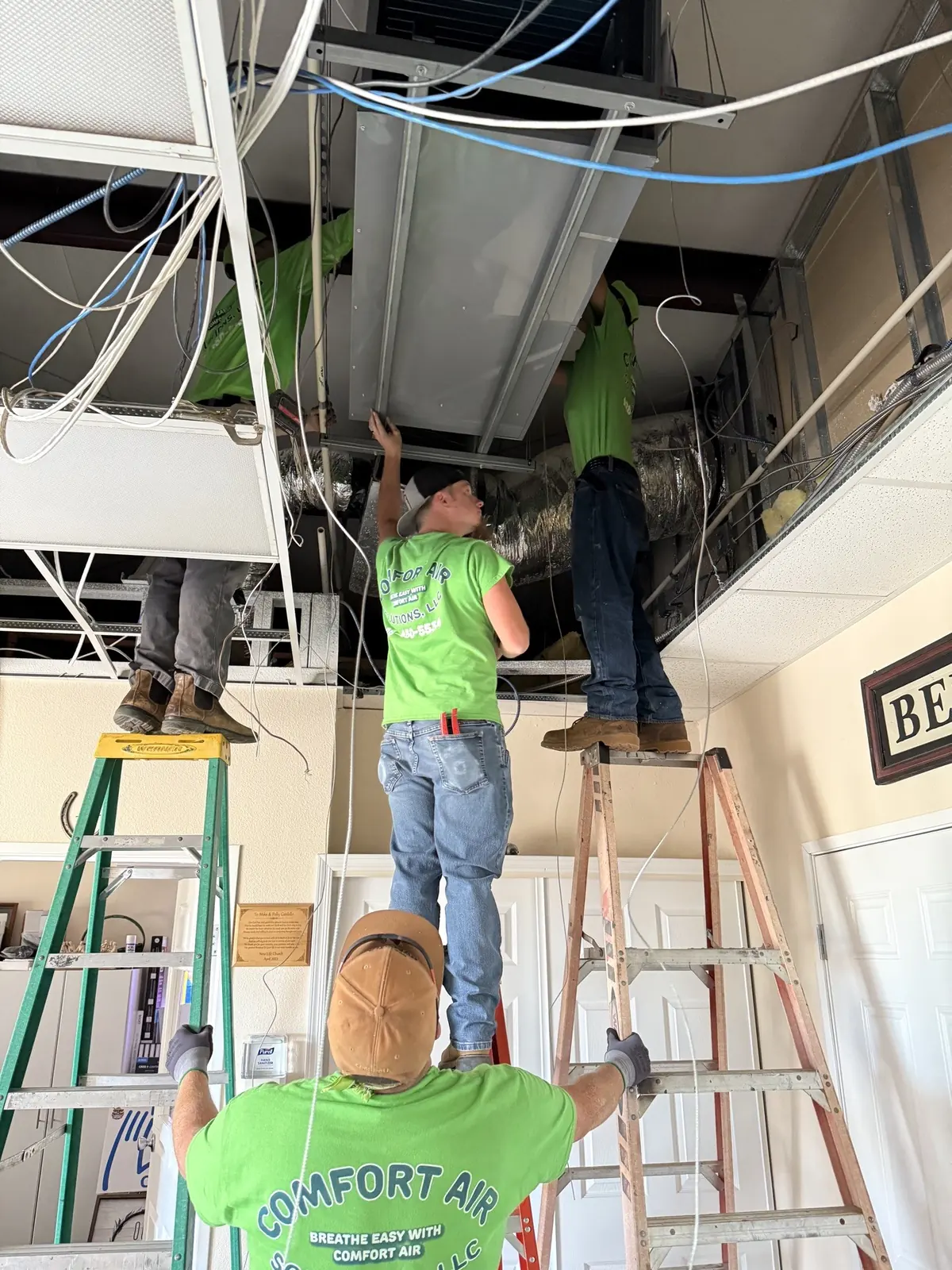Comfort Air Solutions crew on ladders working above an open commercial ceiling